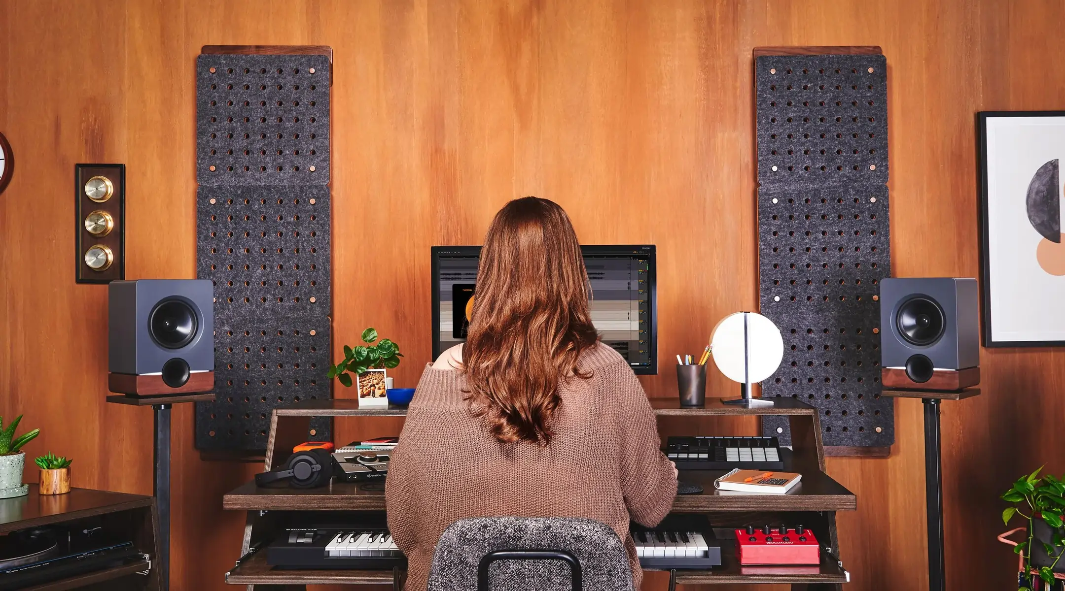 A woman sitting at an Output | DEFI desk in a music production studio with her back to the camera doing audio production work.