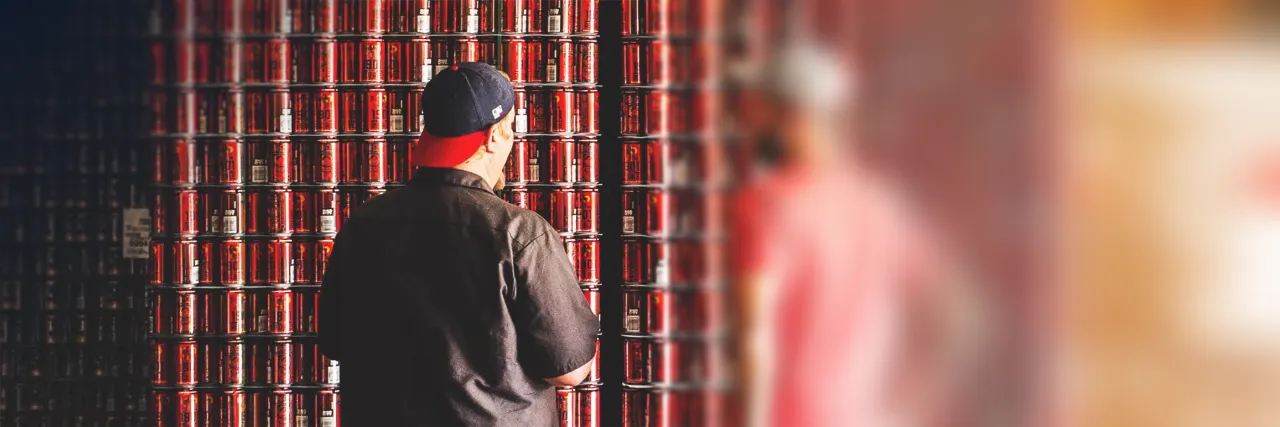 Craftpeak: a brewer in a baseball cap standing in front of a wall of stacked red beer cans.